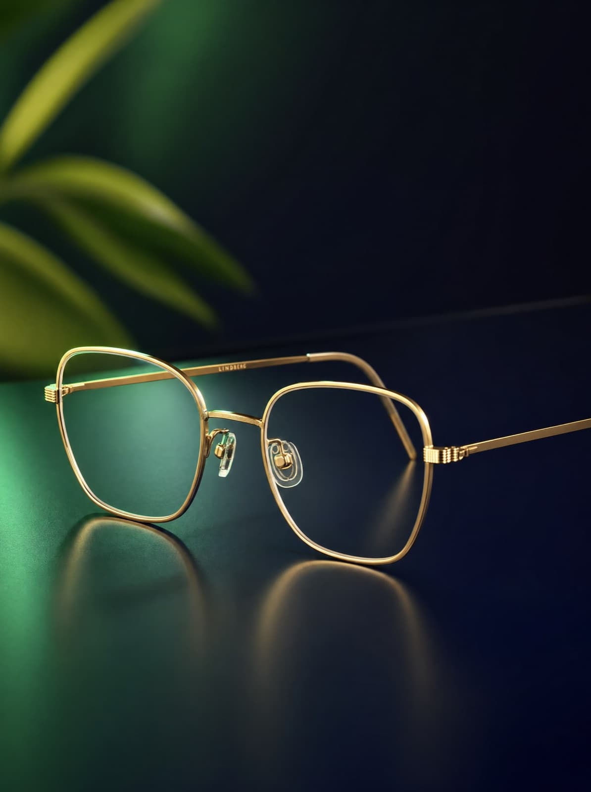 Thin gold-rimmed eyeglasses on a deep navy surface with soft green light